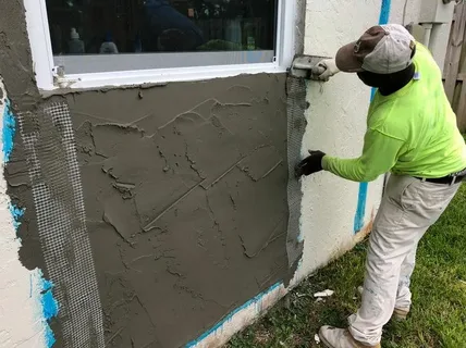 Worker applying stucco to exterior wall during home repair
