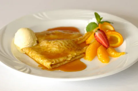 Golden Crêpe Suzette served with ice cream and fresh fruit on a white plate