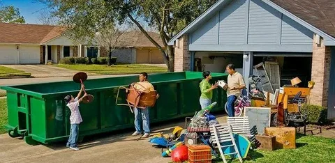 Family loading old furniture into a large green dumpster